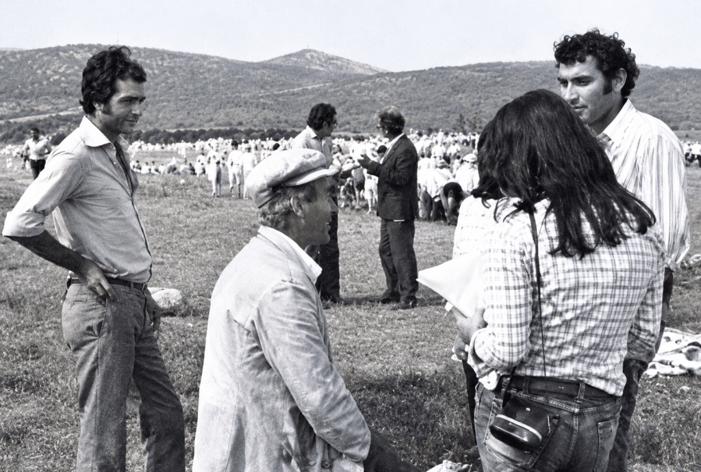 Bir grup insanın açık bir alanda, uzakta hayvan sürüsüyle sohbet ettiği bir siyah beyaz fotoğraf.